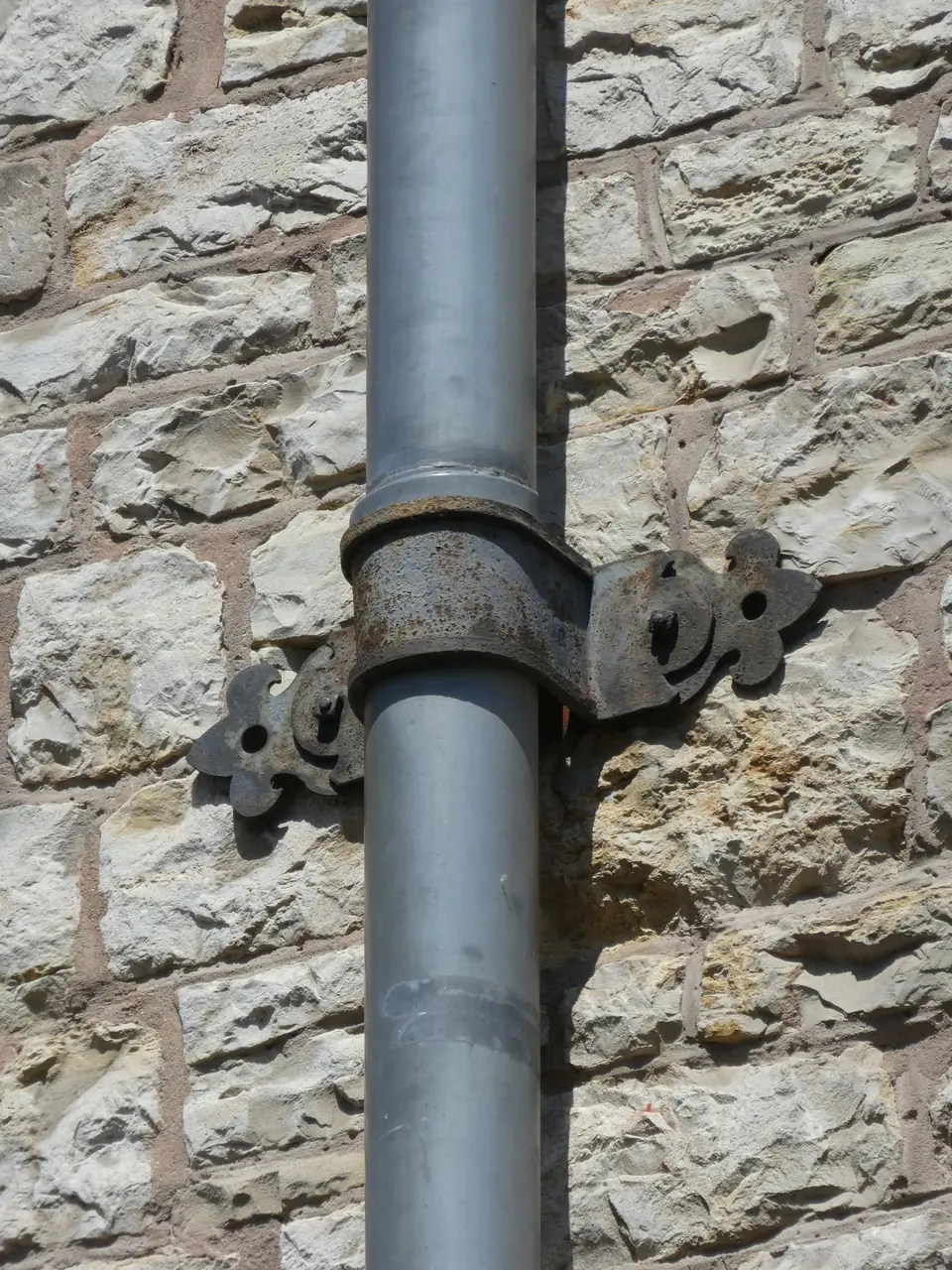 Tuyau de descente d'eaux pluviales fixé par un collier sur un mur en pierre.